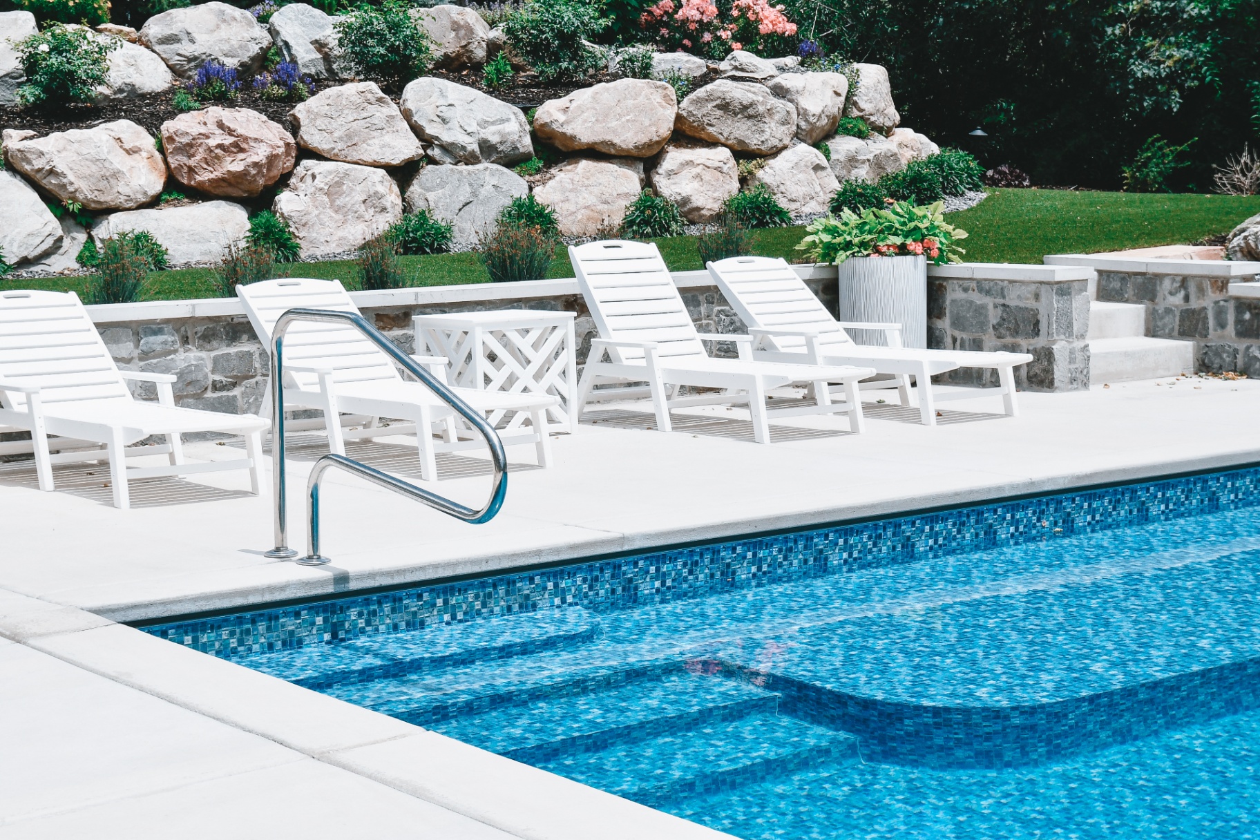 Kaysville Utah Mosaic-Tile Vinyl Pool with Lounge — Barr Pool Builders Blue mosaic-tile inground vinyl swimming pool with poolside lounge chairs and boulder wall in Kaysville, Utah by Barr Pool Builders