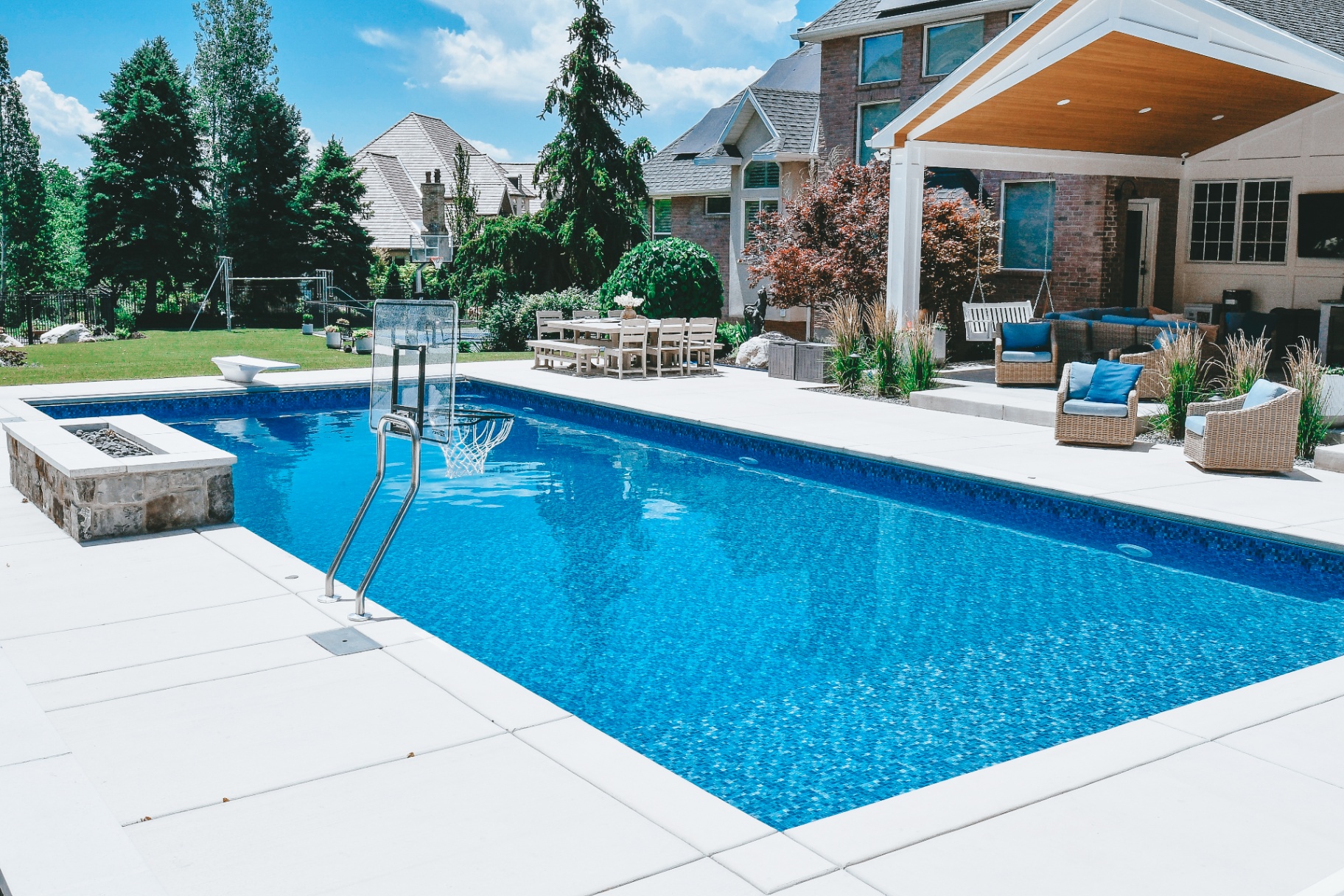 Layton Utah Luxury Vinyl Pool with Basketball Hoop & Firepit — Barr Pool Builders Luxury vinyl swimming pool with in-pool basketball hoop, diving board and stone firepit in a Layton, Utah backyard built by Barr Pool Builders